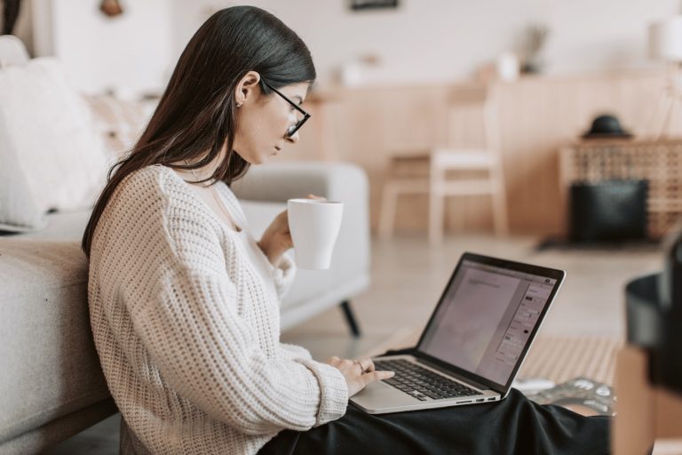 Woman working on her laptop in her living room drinking a coffee